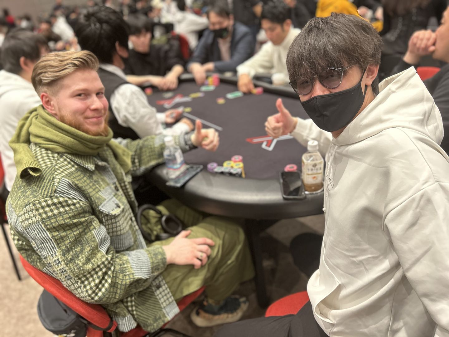 ポーカーテーブルに座っている2人の男性がカメラに向かって微笑んでいる様子
